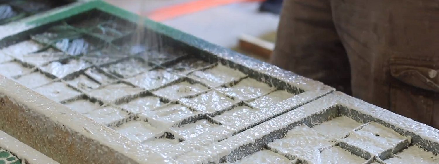 Close-up of clear sealer being poured across a cast concrete mosaic tile panel, bringing up a high shine.