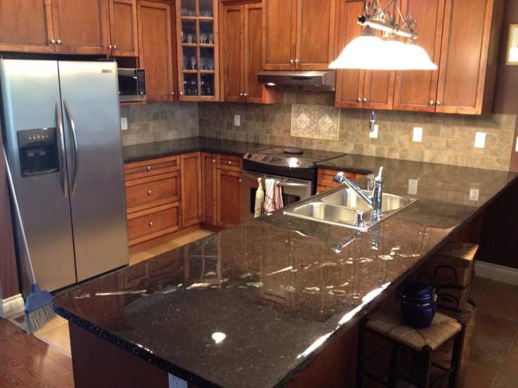 A kitchen island and counters finished in near-black concrete with fine light speckling and a high-gloss seal, with timber cabinets and a stainless sink.