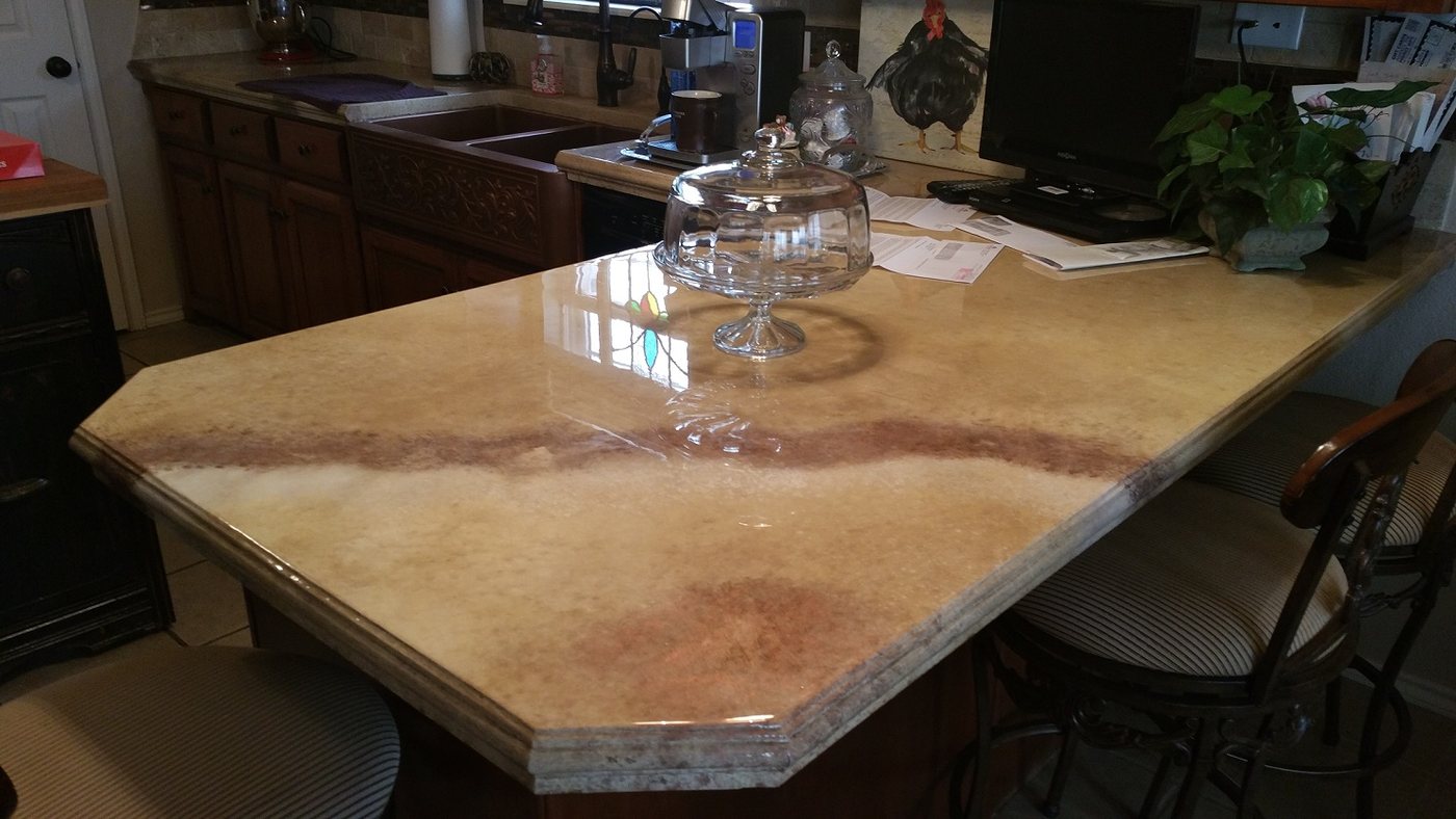 A long concrete bar top in cream and pale gold with a rust-coloured vein running across it, polished glossy, with a clipped corner and bar stools alongside.