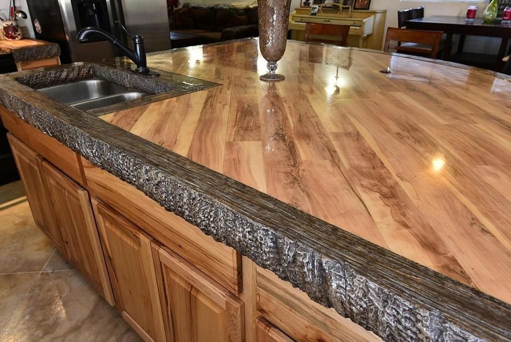 A large kitchen island with a concrete countertop finished to look like wide timber planks, with a heavily chiselled dark stone edge and an undermount sink.