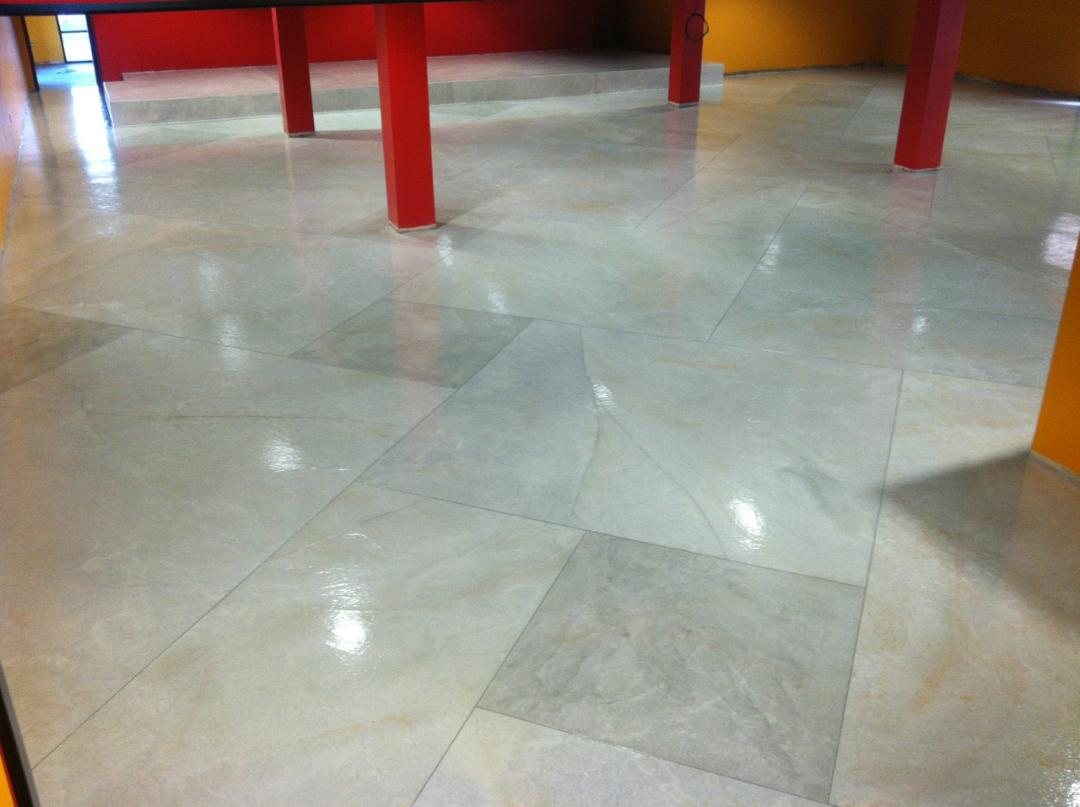 A large pale marbled concrete floor in a commercial interior with bright red columns, panels laid at varying angles and polished to a high gloss.