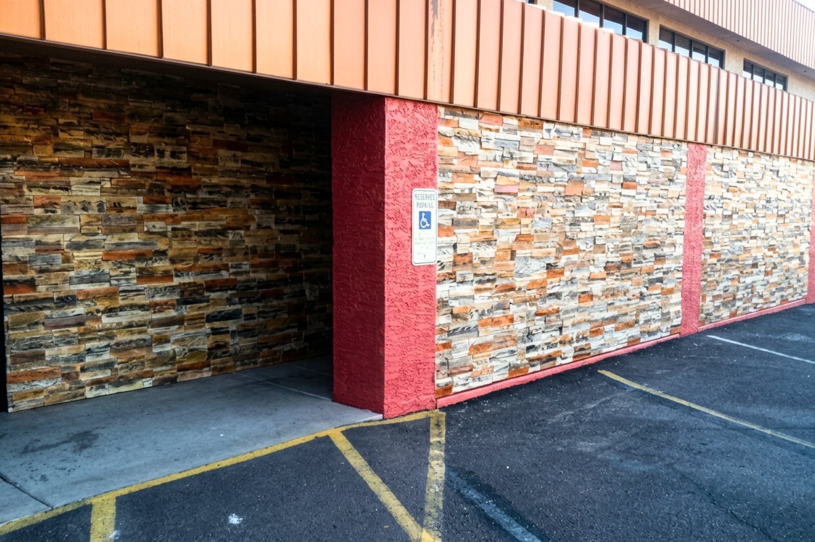 A commercial building frontage clad in two different tones of stacked stone veneer either side of a red painted column, seen from the car park.