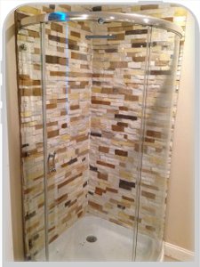 A curved glass shower enclosure with the interior walls clad in multi-coloured gold, cream and brown stacked stone panels.