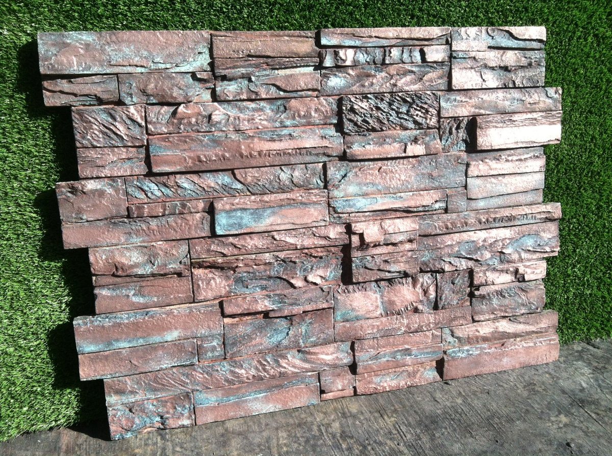 A concrete wall panel coloured in dusky pink and blue-green, leaning against artificial turf.