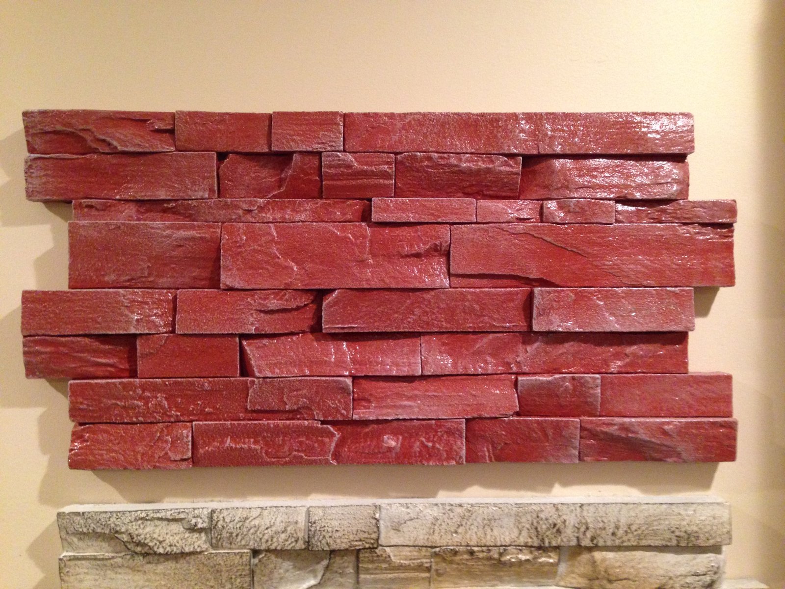 A close-up of a barn red stacked stone concrete panel mounted on a wall above a cream panel, showing individual split stone faces.