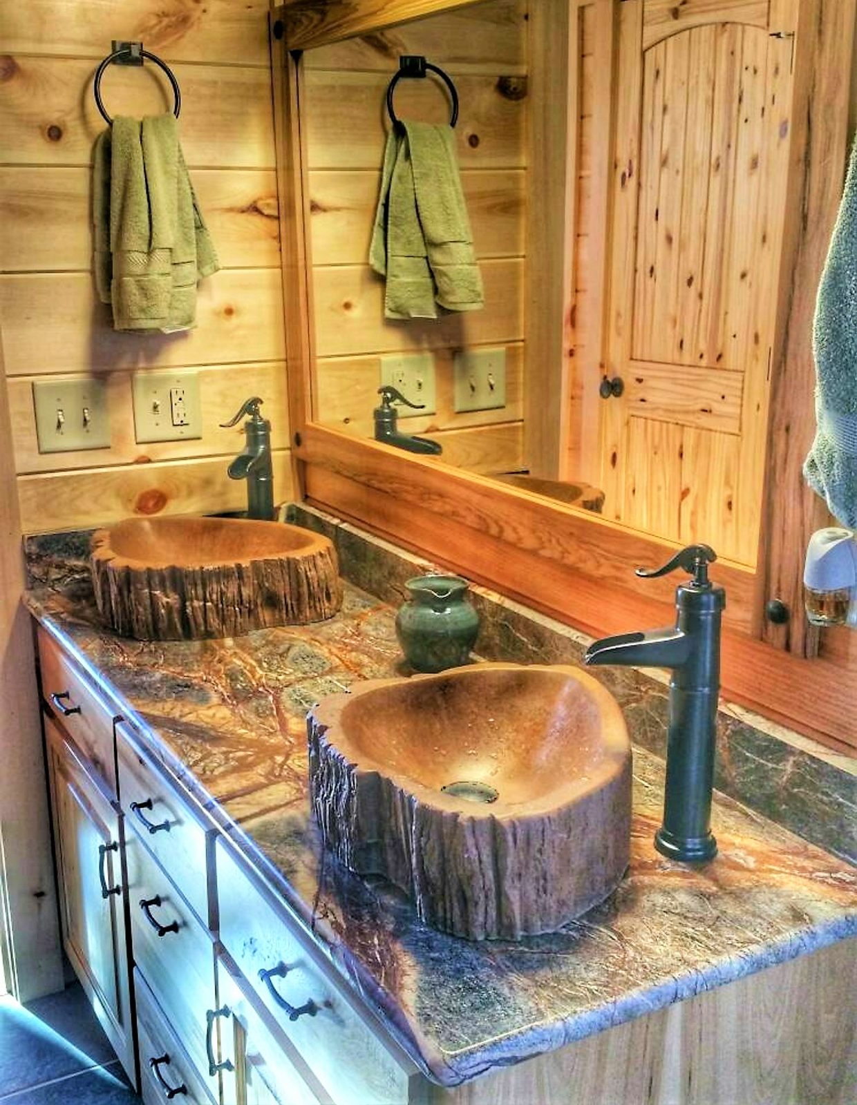 A log-cabin bathroom with a concrete double vanity and two petrified-wood concrete vessel sinks with bronze faucets.